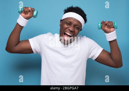 Smiling young african american guy training with dumbbells. Stock Photo