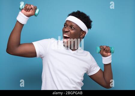 Smiling young african american guy training with dumbbells. Stock Photo