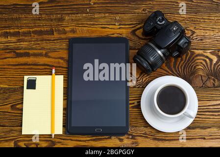 Black tablet computer on a old wooden table with a mug of coffee, camera and notebook with pencil Stock Photo
