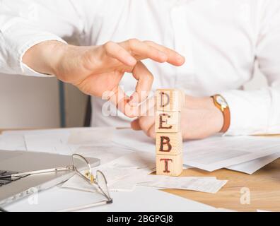 Businessman removes wooden blocks with the word Debt. Reduction or restructuring of tax. Bankruptcy announcement. Refusal to pay loans and invalidate Stock Photo