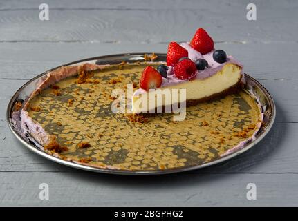 Last slice of home made Cheesecake with berries on plate on grey wooden background. Stock Photo