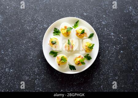 Stuffed eggs with egg yolk, bacon, mustard and parsley on dark stone background with copy space. Top view, flat lay Stock Photo