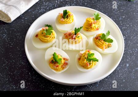 Stuffed eggs with egg yolk, bacon, mustard and parsley on white plate Stock Photo