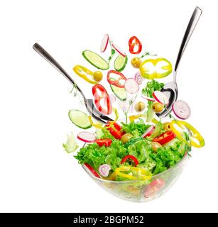 Flying vegetable salad ingredients over transparent bowl with spoons isolated on white. Healthy balanced food concept. Stock Photo