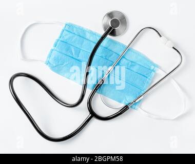 Stethoscope on blue protective mask on white background. Family doctor. Flat lay Stock Photo