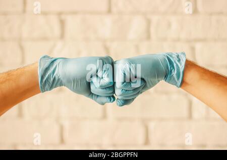 Two men bumping hands in blue medical gloves as protection against coronavirus. Doctor surgeons in blue protective latex gloves clapping fists. COVID- Stock Photo