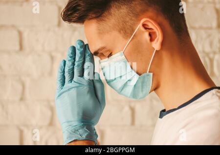 Religious doctor in protective gloves and medical mask praying for help to God in hospital. Young sick man prayer in medical gloves on hands and prote Stock Photo