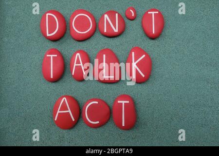 Don't talk, act, motivational sentence composed with red colored stone letters over green sand Stock Photo