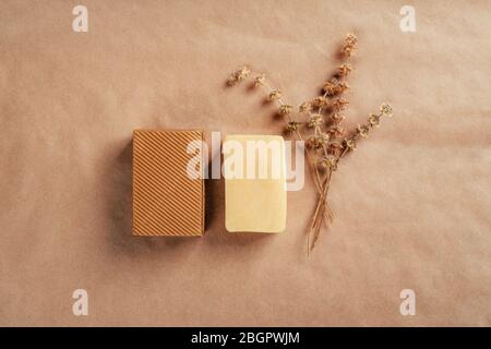 Piece of soap with ruffle carton box and dry herbs on rustic natural paper. Health and beauty concept. Stock Photo