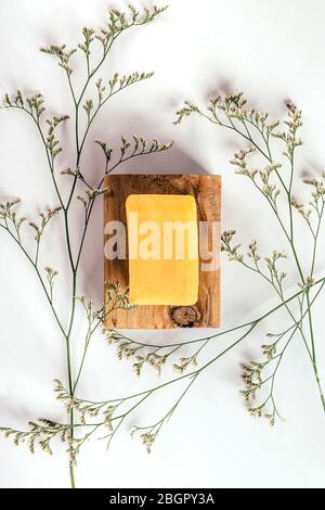 Piece of soap on wooden bar and herbs around on white paper background. Health and beauty concept. Stock Photo