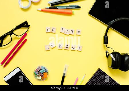 Online education concept. Tablet, phone, headphones, notebook, school supplies on yellow background. Distance school in quarantine. View from above wi Stock Photo