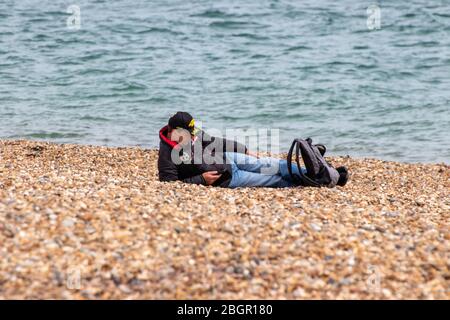 A middle aged man laying alone on a pebble beach in spring Stock Photo