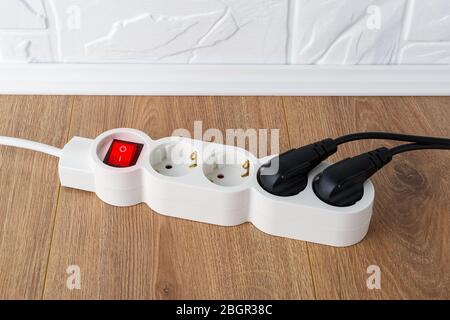 White extension cord with power button and four outlets on the floor. Electric power strip with switch for home or office. Household appliances. Stock Photo