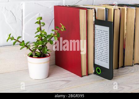 E-reader on a shelf with paper books and small potted plant. Copy space on e-book display. E-reading for pleasure and education. Front view. Stock Photo