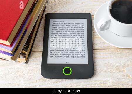E-reader, stack of ordinary paper books and cup of coffee on a white wooden table. Copy space on e-book display. E-reading for pleasure and education. Stock Photo