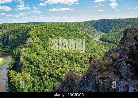 A man climbs a mountain on a background of a river valley. Stock Photo