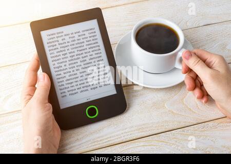 Woman hands hold e-reader and cup of hot coffee over a white wooden table . Copy space on e-book display. E-reading for pleasure and education. Stock Photo