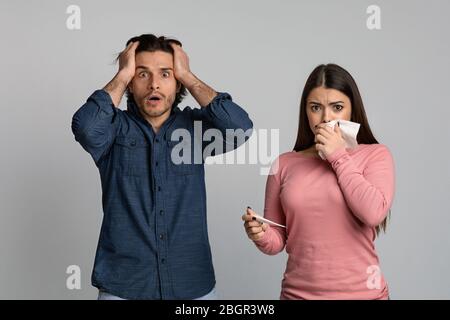 Coronavirus Symptoms Panic. Shocked Man Standing Next To His Sick Girlfriend Stock Photo