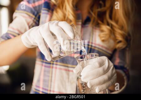 Close up of female hands in gloves holding bottle and glass, pouring pure water. Healthy lifestyle, health care, diet. Preparing, proposing for somebody. Copyspace. Water purification, safety. Stock Photo