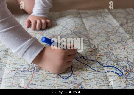 Hand of the child writing on a map with blue pen. Kids hand holding felt-tip pen. Travel and vacation  with children. Summer rest concept. Stock Photo