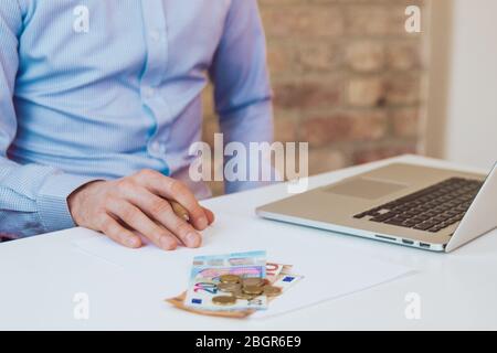 Man sitting at a desk with laptop and reading papers in light blue shirt. Light workspace, business space. Working environment. Brick wall background. Stock Photo