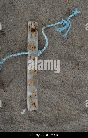 A piece of worn blue nylon rope attached to a piece of weathered wood lies on a sand beach in Nova Scotia, Canada Stock Photo