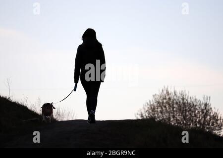 Silhouette of a girl walking a dog on a leash on a hill. Care for a pet during coronavirus pandemic, spring weather Stock Photo