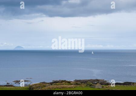 Single yacht in Scottish landscape with in the background Ailsa Craig island in the Firth of Clyde south of the Isle of Arran, Scotland Stock Photo