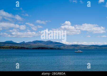 Moored yacht with Isle of Arran in distance viewed from Kintyre, Argyll coast, Scotland Stock Photo