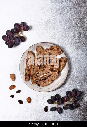 Top view of sliced rusk fruit bread on a plate with red grapes, rosins and almond nuts. Homemade healthy food concept.  Copy space. Stock Photo