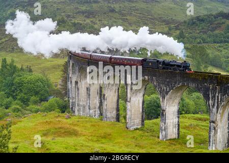 'The Jacobite' locomotive steam train on West Highland Rail crosses famous Glenfinnan Viaduct tourist spot in the Highlands of Scotland Stock Photo