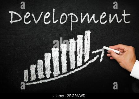 Blackboard with handwritten development text. Arrow going upwards and stack chart. Development and progress concept. Stock Photo