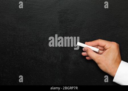 Male hand with chalk on the wall of black paint. White shirt. Ideal for any communications or advertising Stock Photo