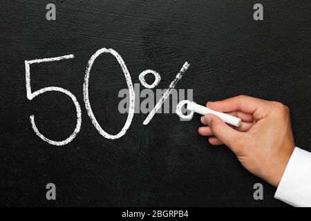 Fifty percent discount or increase. Blackboard with text in numbers 50% reduction or increase. Hand with chalk in hand ending writing. Stock Photo