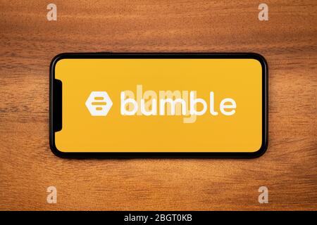 A smartphone showing the Bumble logo rests on a plain wooden table (Editorial use only). Stock Photo