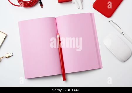 open pink paper notebook, power bank with cable, red smartphone, headphones, wireless mouse on white background, workplace, top view, flat lay Stock Photo