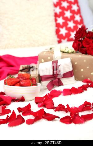 Romantic still life with strawberry, gift boxes and petals of roses on bed Stock Photo