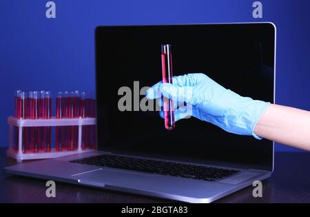 Scientist entering data on laptop computer with test tubes in a laboratory on blue background Stock Photo