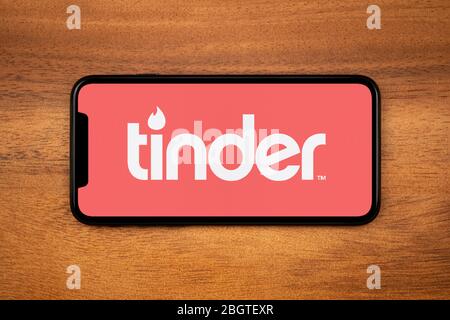 A smartphone showing the Tinder logo rests on a plain wooden table (Editorial use only). Stock Photo