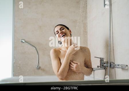 Happy woman enjoying,having a rejuvenating cold shower,singing.Bathroom personal hygiene routine.Self care.Body,hair,skin care cosmetics.Relaxing home Stock Photo