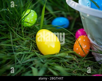 Colorful Easter eggs in grass next to a basket full of polka dotted eggs Stock Photo