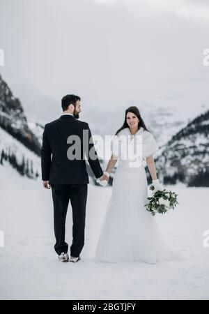 bride smiles while holding hand of groom in winter on frozen lake Stock Photo