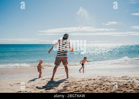 Kids playing with water at the beach with their dad on a sunny day Stock Photo