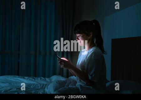 Asian mobile addict woman using smaryphone browsing the internet for watching movie or virtual meeting video call online with boyfriend on the bed bef Stock Photo