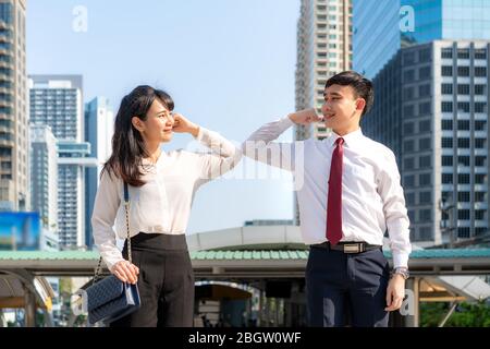 Elbow bump is new novel greeting to avoid the spread of coronavirus. Two Asian business friends meet in front of office building. Instead of greeting Stock Photo