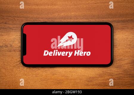 A smartphone showing the Delivery Hero logo rests on a plain wooden table (Editorial use only). Stock Photo