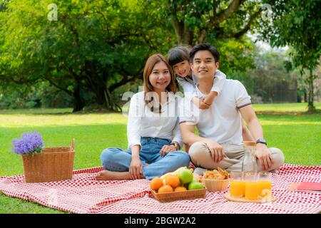 Asian teen family happy holiday picnic moment in the park with father, mother and daughter looking at camera and smile to happy spend vacation time to Stock Photo