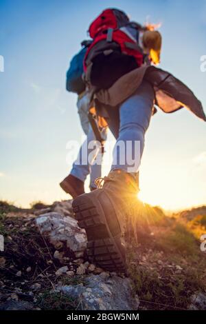 Tourist couple wearing hiking boots walk up a grassy hill in Alps. Stock Photo