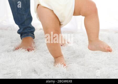Cute baby boy taking first steps with mother in room Stock Photo