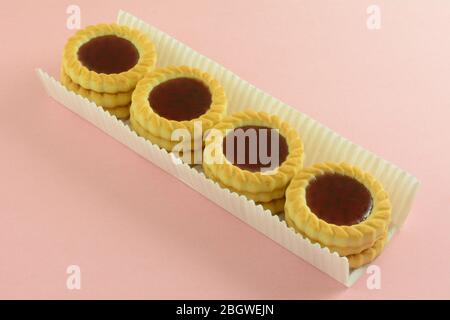 Close up of red raspberry fruit tartlette cookies in paper packaging to prevent breakage on pink background Stock Photo